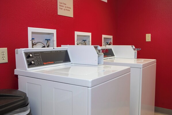 A laundry area with three washing machines, a control panel, and a sign indicating cycle times.