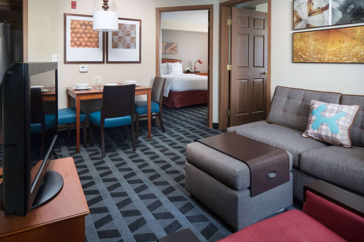 A hotel room with a TV, a desk with a chair, a sofa, and a bed.