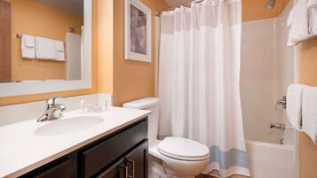 A bathroom with a white sink, a toilet, a shower with a white curtain, and a mirror above the sink.