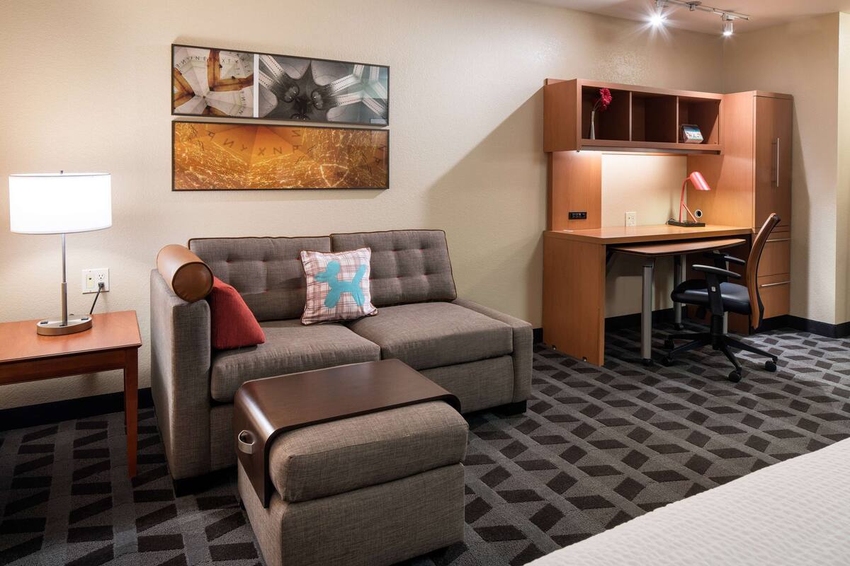 A hotel room with a sofa, a desk, a lamp, and a bed.