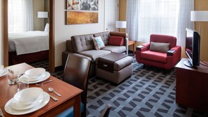 A hotel room with a bed, a sofa, a red armchair, a television, and a dining area with plates and glasses. - Sonesta Simply Suites Seattle Renton (Renton)