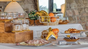 Ein reichhaltiges Frühstücksbuffet mit verschiedenen Speisen, darunter Obst, Gebäck und Fleisch, auf einem Tisch mit einer Lampe und einer Steinwand im Hintergrund.