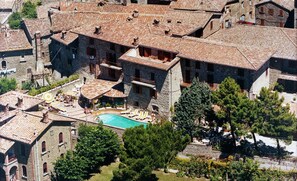 A stone building with a swimming pool, surrounded by trees and other buildings. - Relais La Fattoria (Passignano sul Trasimeno)