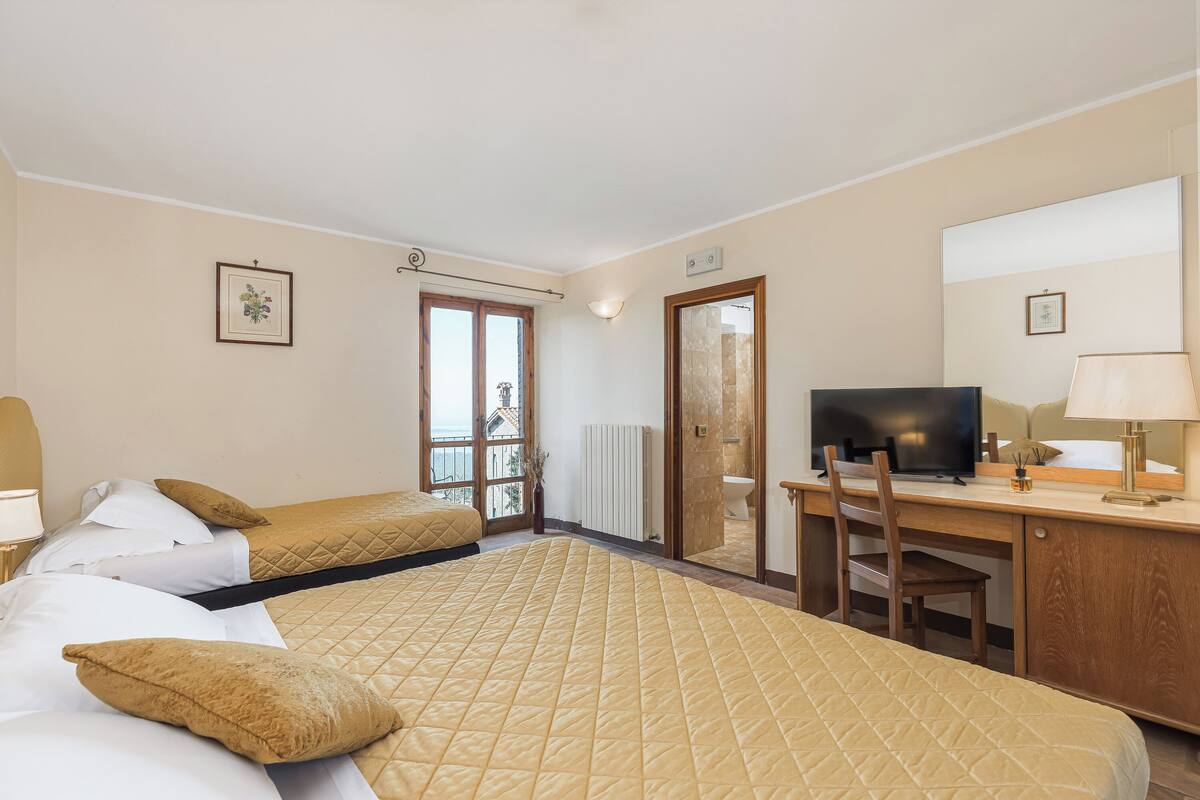 A hotel room with two beds, a desk with a television, a chair, and a window with a view.