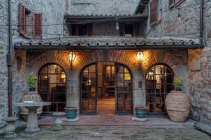 Un edificio de piedra con ventanas de arco y techo de tejas. Hay macetas grandes y una mesa pequeña afuera.