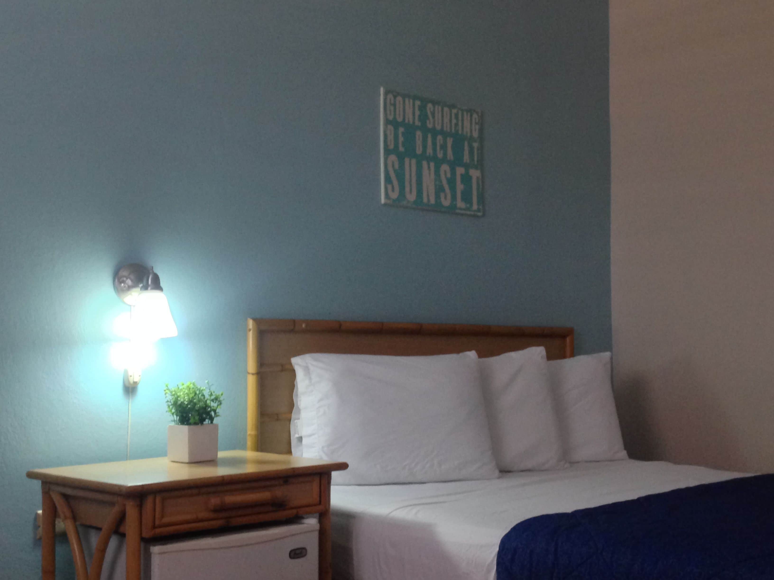 Un dormitorio con cama, mesita de noche, lámpara y un cartel en la pared.