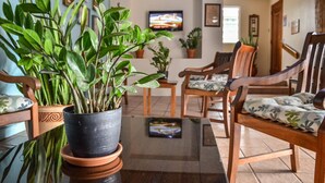 A living room with a large potted plant, wooden chairs, a television, and a tiled floor. - Parador Boquemar (Cabo Rojo)