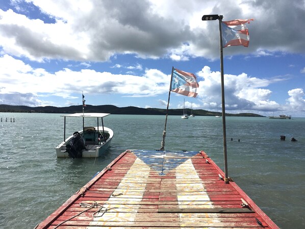 A wooden pier with a flag, boats, and a distant island. - Parador Boquemar (Cabo Rojo)