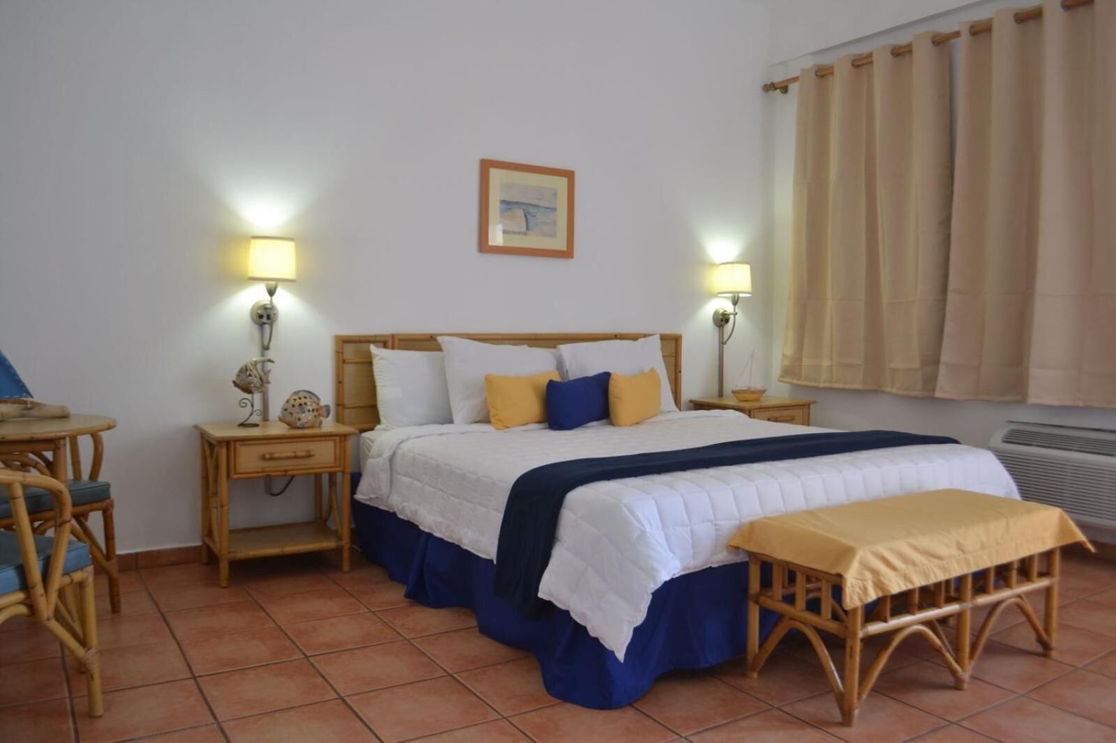 Un dormitorio con una cama, mesitas de noche, una silla, un banco y un cuadro en la pared.