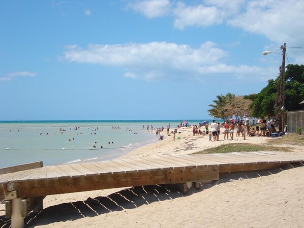 A beach with a wooden boardwalk leading to the shore, populated with people and umbrellas. - Parador Boquemar (Cabo Rojo)