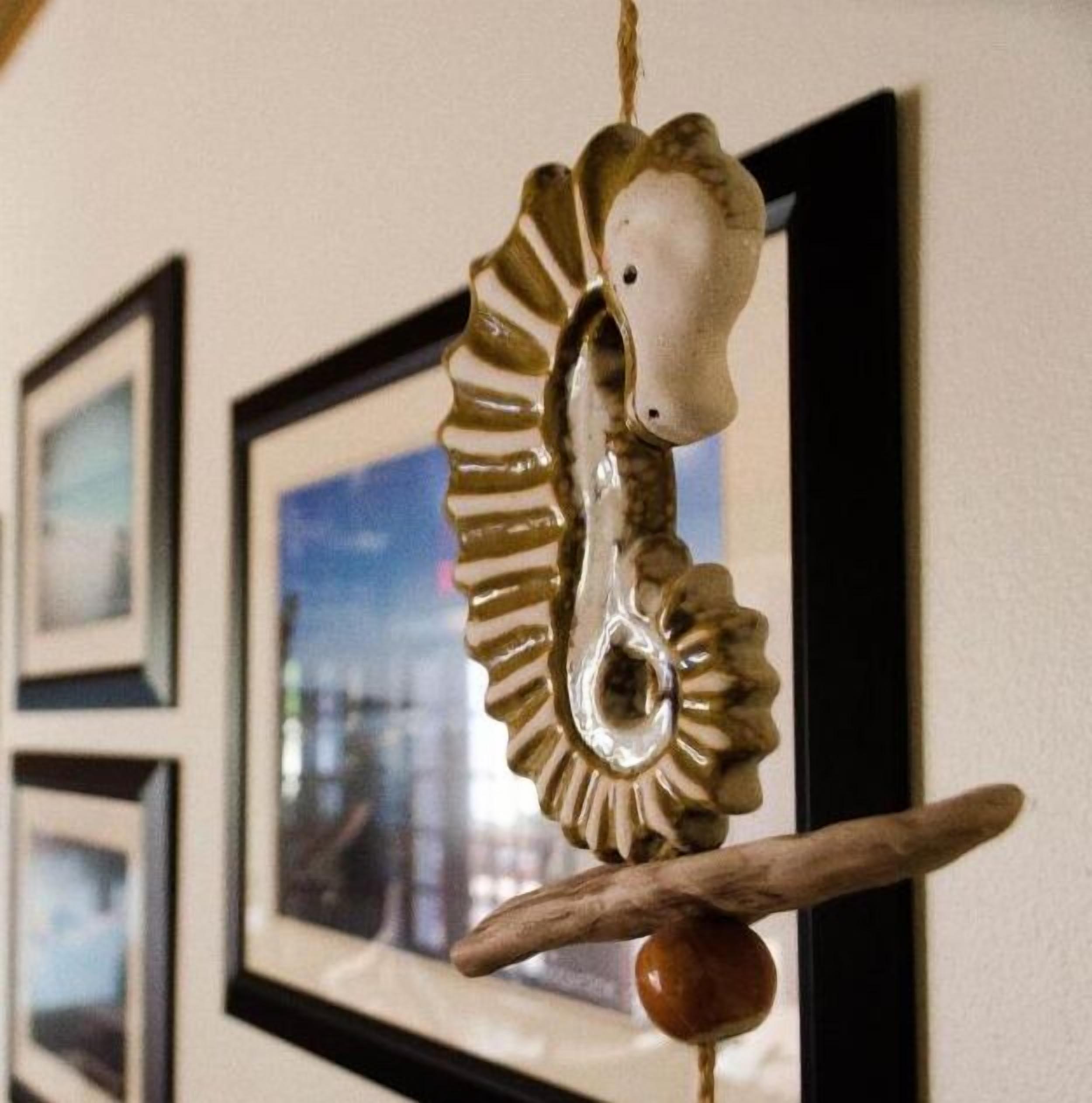 A seahorse decoration hanging on a wall with framed pictures in the background.