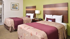 A hotel room with two beds, each with a wooden headboard, a nightstand with a lamp, and a framed picture on the wall.