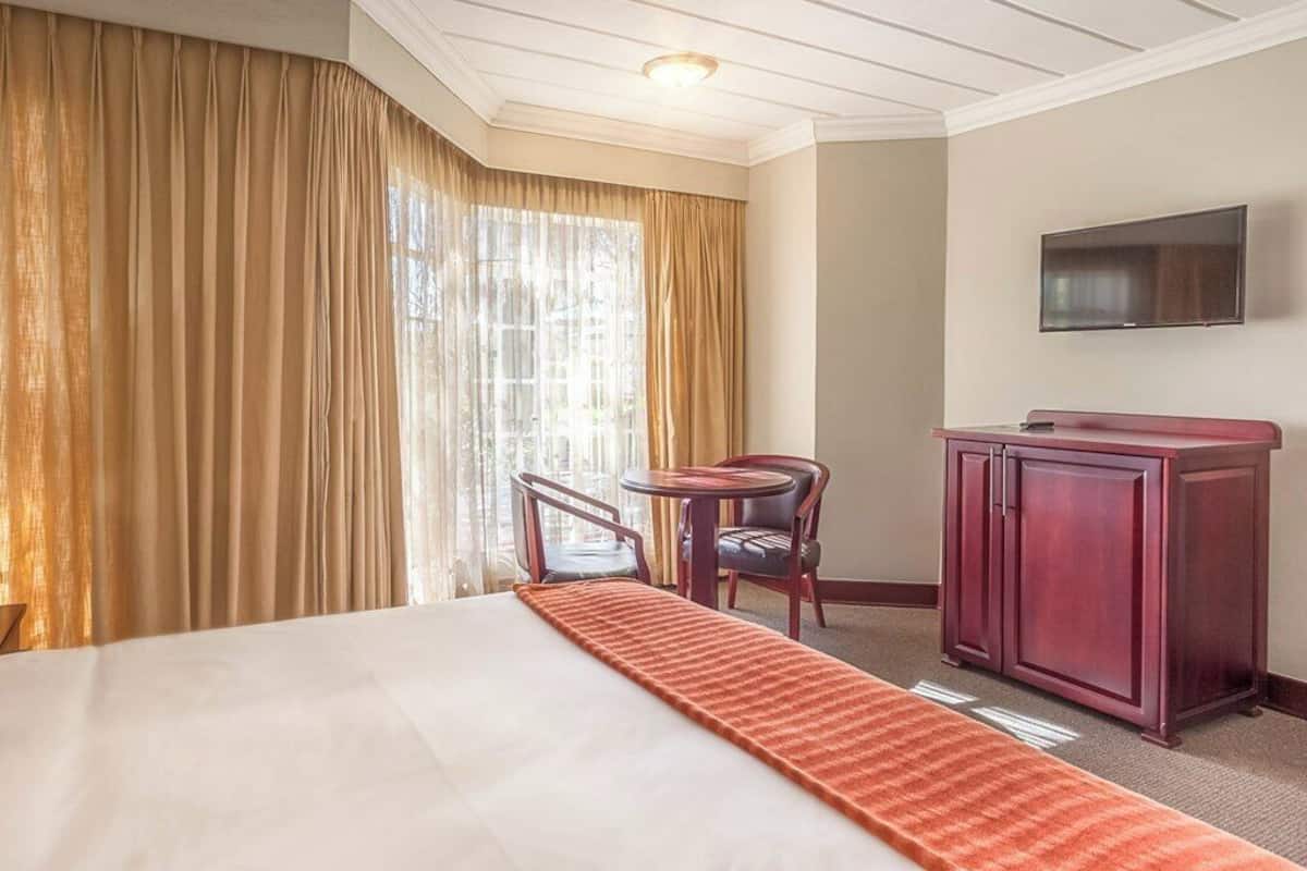 Une chambre d’hôtel équipée d’un lit, d’un bureau, d’une chaise, d’une télévision et d’une grande fenêtre avec des rideaux.