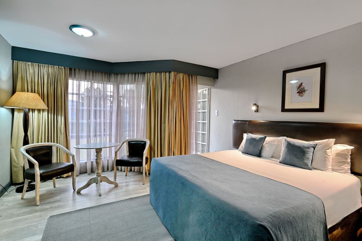 Une chambre d’hôtel avec un grand lit, deux chaises, une petite table et une fenêtre avec des rideaux.