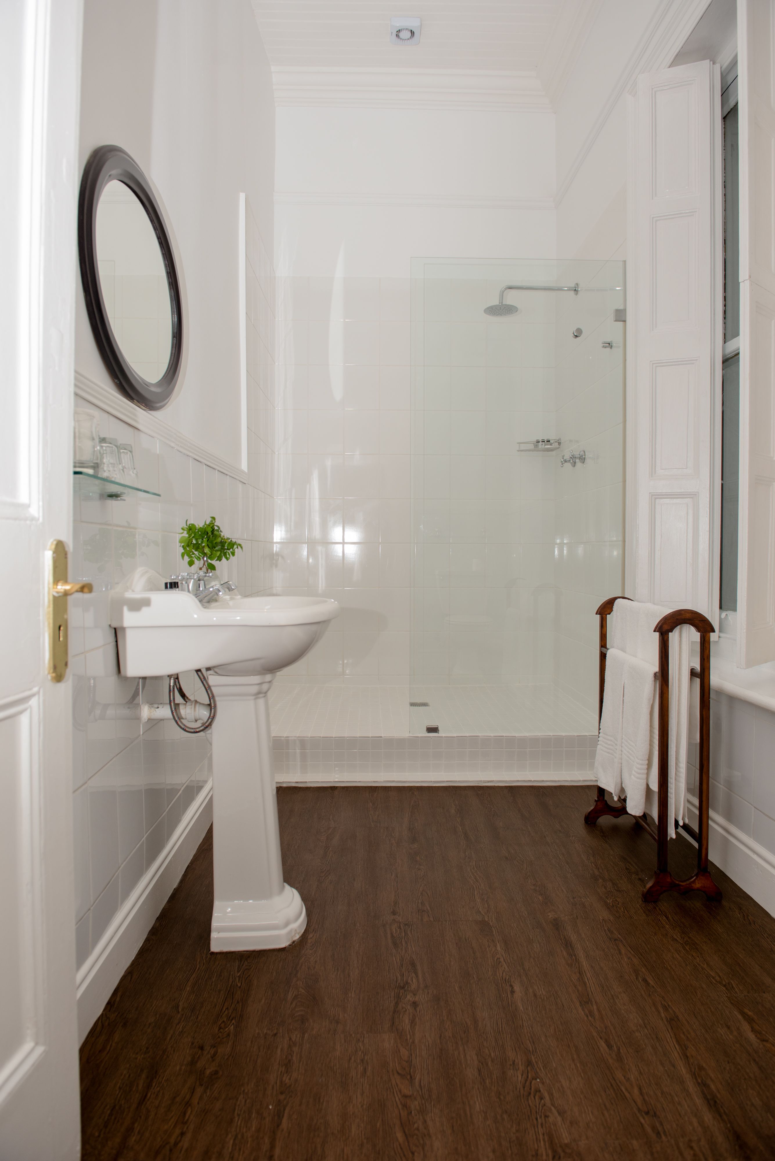 A bathroom with a white pedestal sink, a glass shower enclosure, and a wooden towel rack.