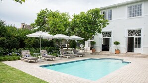 Une piscine rectangulaire, bordée d’une terrasse carrelée, entourée de chaises longues et de parasols.