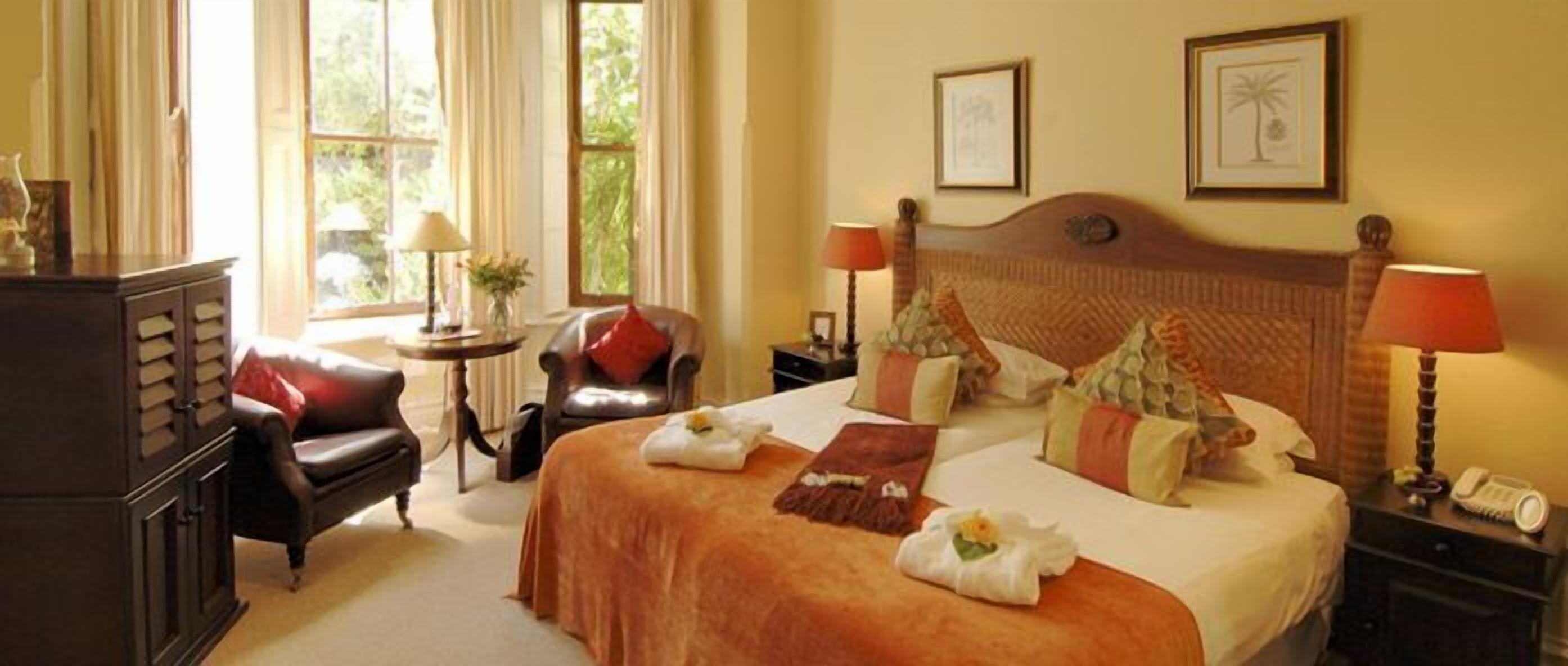 A hotel room with a large bed, two bedside tables, a nightstand, a desk, a chair, and a window with curtains.