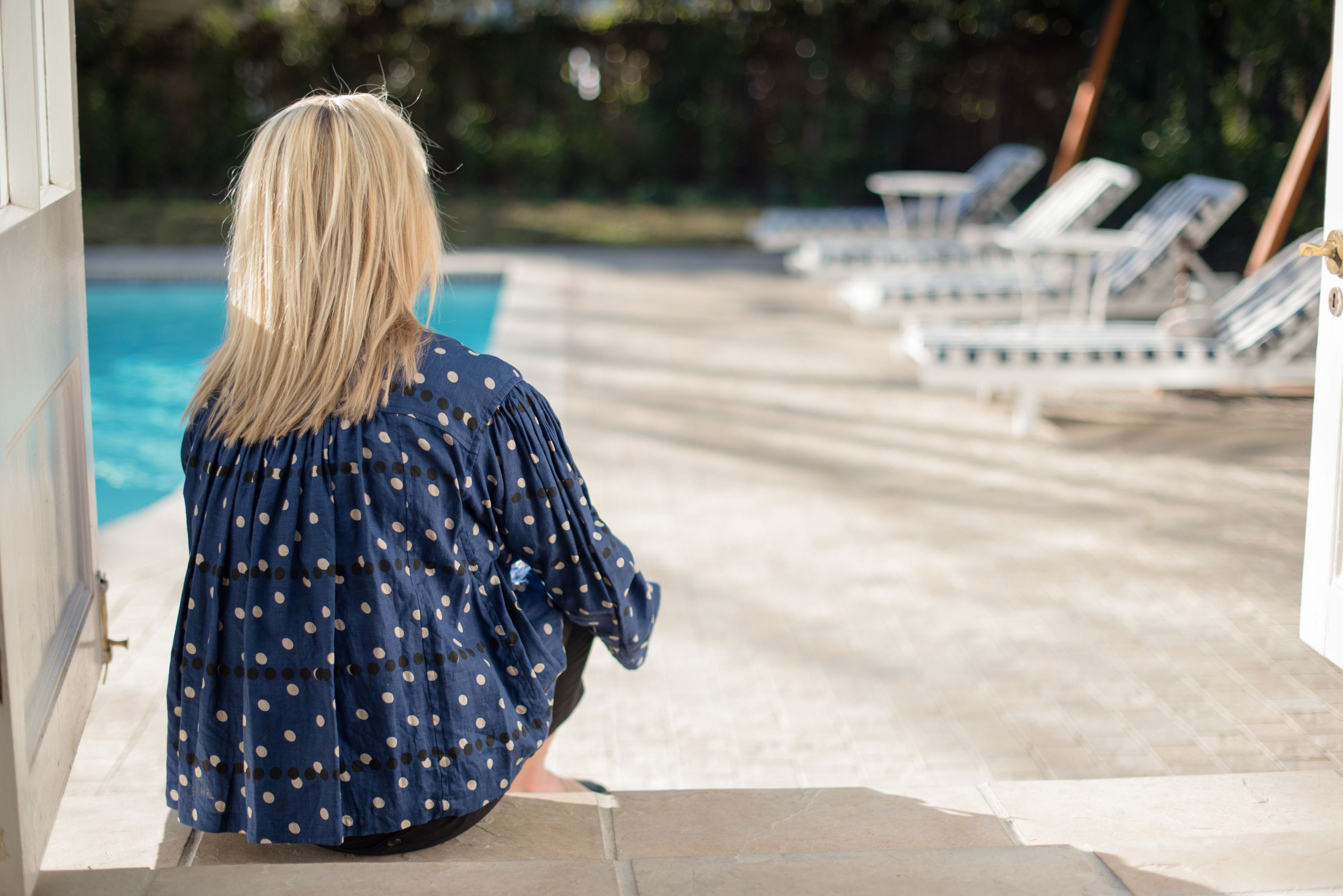 A person sitting by a poolside with lounge chairs in the background.