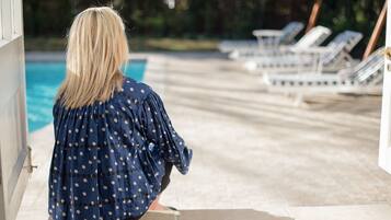 A person sitting by a poolside with lounge chairs in the background.