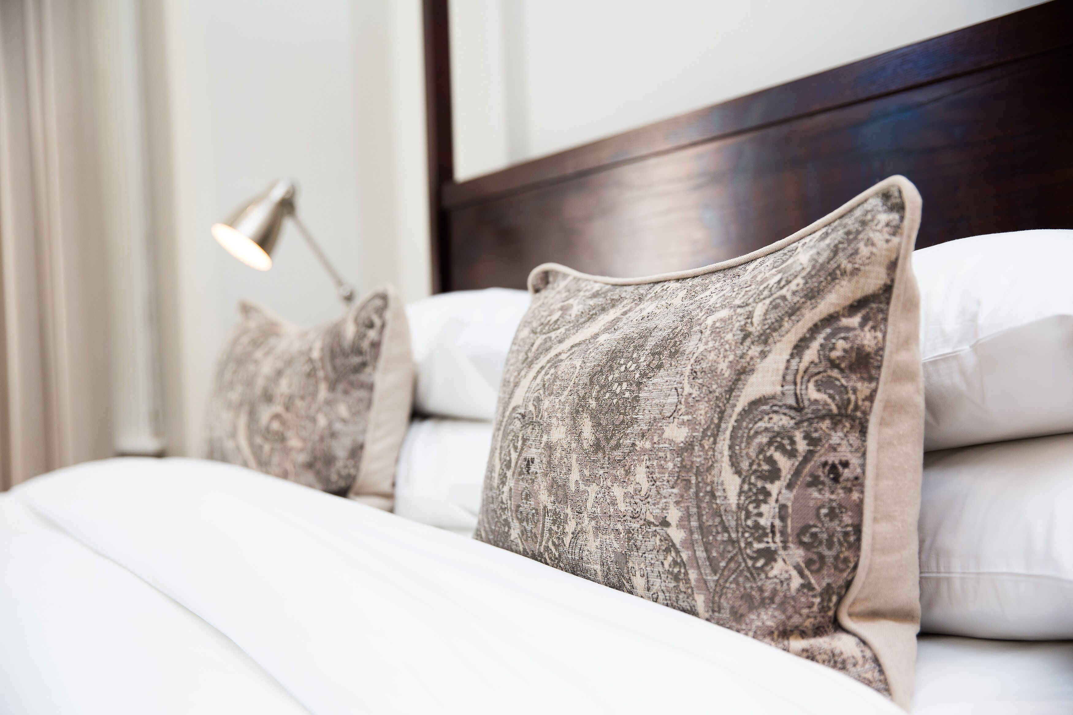 A neatly made bed with patterned pillows and a bedside lamp.