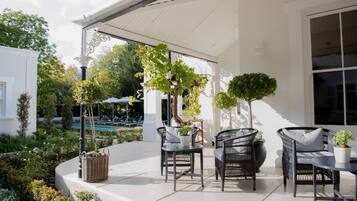 An outdoor patio with wicker furniture, potted plants, and a pool in the background.