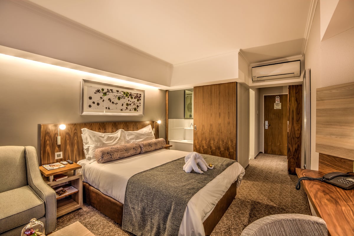 Una habitación de hotel con cama, mesita de noche, lámpara y un cuadro en la pared.