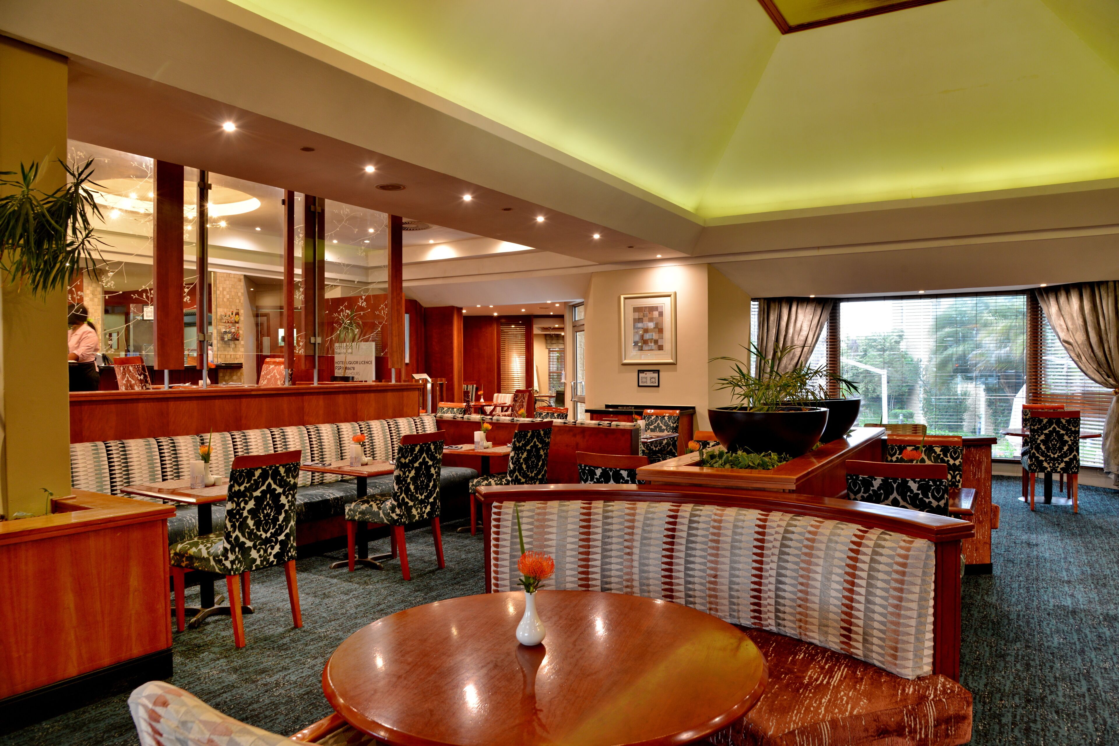 Een hotel lobby met een ronde centrale tafel, zithoeken en een groot raam met uitzicht.