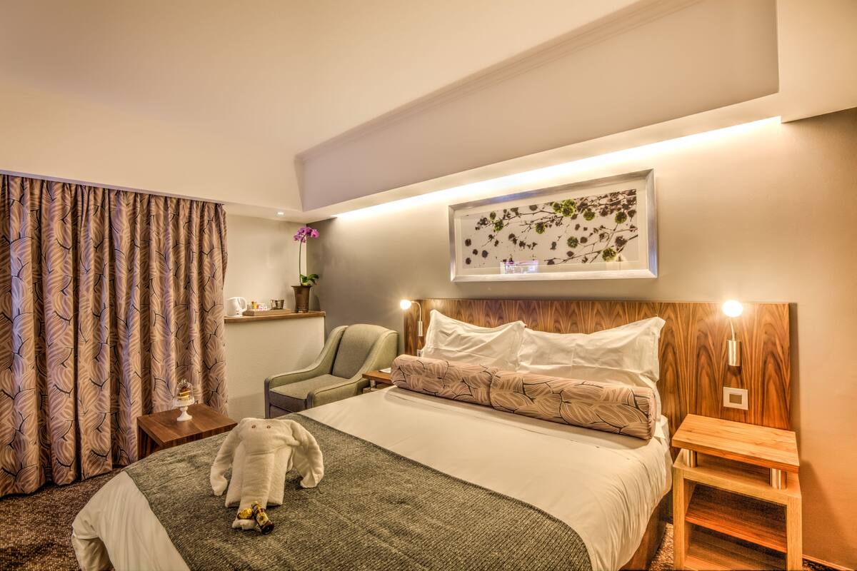 Una habitación de hotel con una cama grande, una silla, una mesita de noche y un cuadro colgado en la pared.
