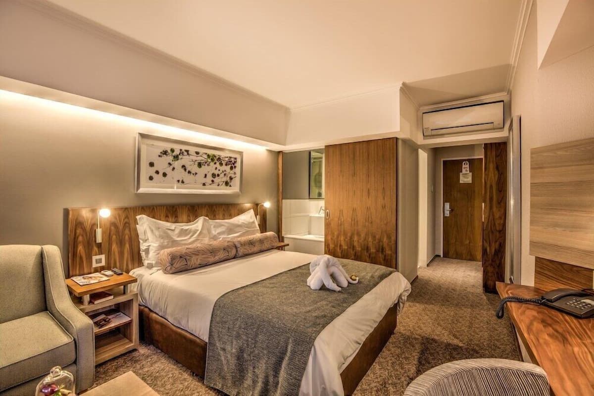 Una habitación de hotel con una cama grande, mesita de noche, lámpara y una obra de arte enmarcada en la pared.