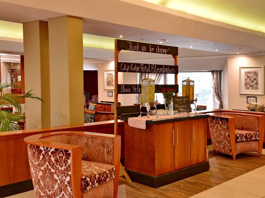 Un hall d’hôtel avec des meubles en bois, un comptoir de réception et une enseigne sur laquelle on peut lire : « Merci d’avoir choisi l’hôtel City Lodge Bloemkantoor. »