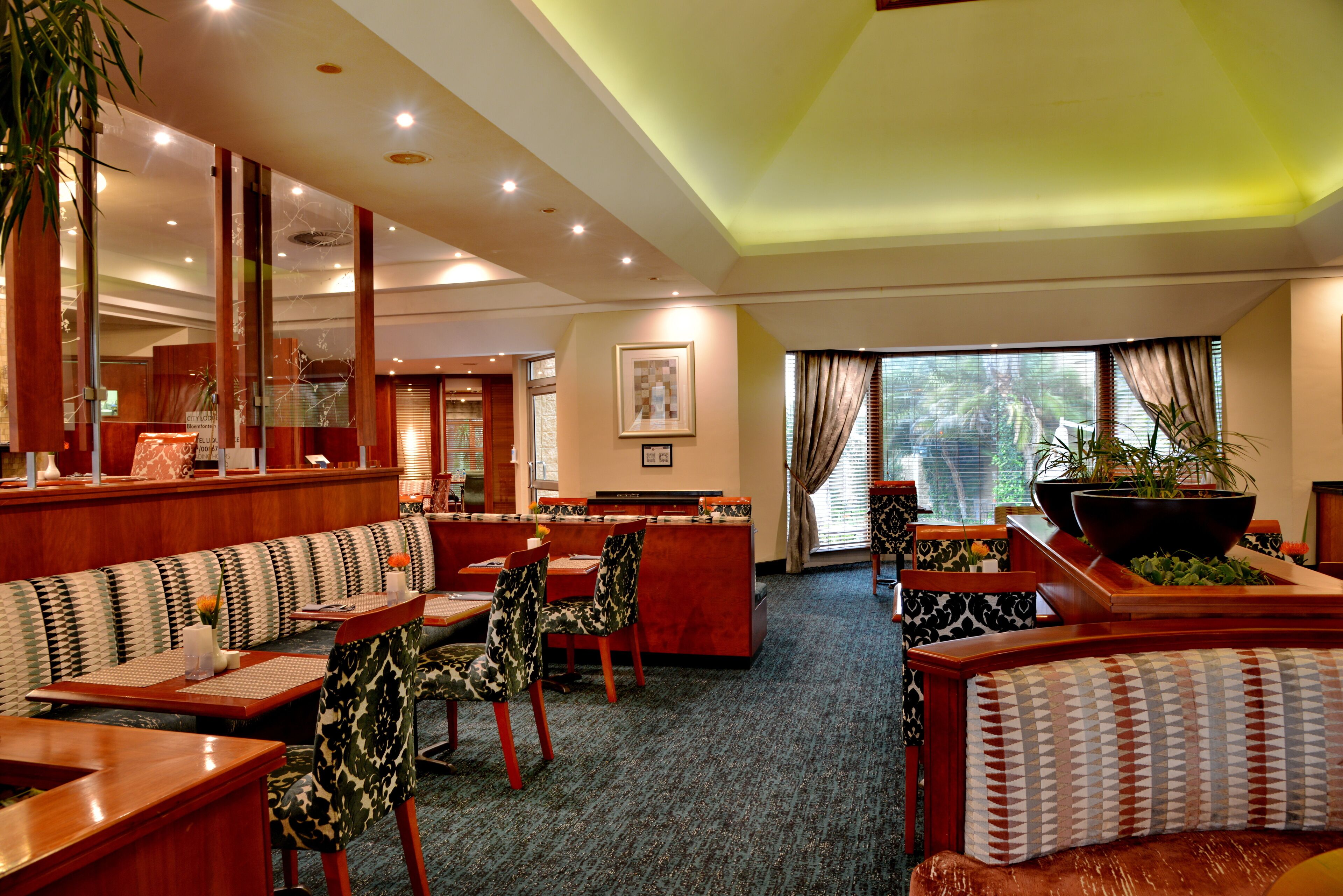 Un vestíbulo de hotel con zonas de estar, un mostrador de recepción y grandes ventanales con cortinas.