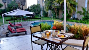 A patio area with a table set for breakfast, including plates, cups, and a vase of flowers.