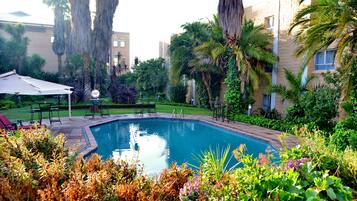 Una piscina rodeada de exuberante vegetación y un patio con mobiliario exterior.