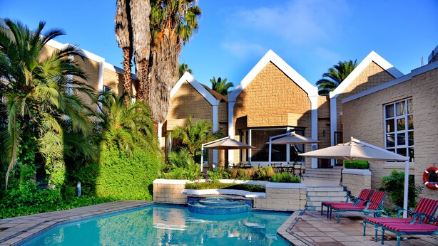 A swimming pool with lounge chairs and umbrellas, surrounded by lush greenery and palm trees.
