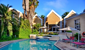 A swimming pool with lounge chairs and umbrellas, surrounded by lush greenery and palm trees. - City Lodge Hotel Bloemfontein (Bloemfontein)