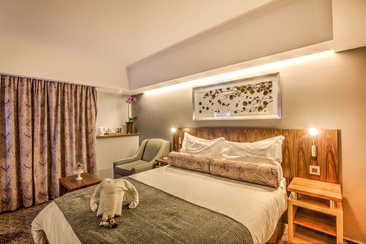 Habitación de hotel con cama, una silla, una mesita pequeña, una mesita de noche y un adorno en la pared.