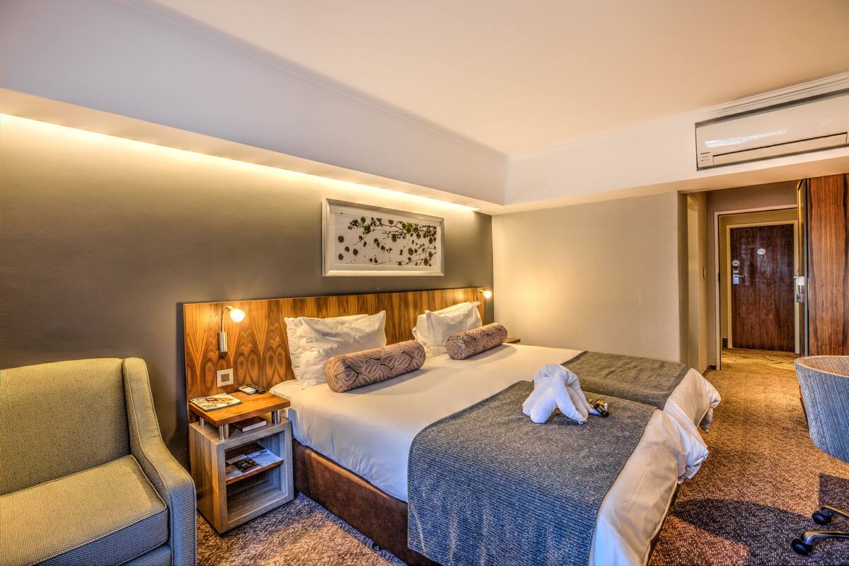 Una habitación de hotel con una cama grande, una mesita de noche con lámpara, una silla y un cuadro en la pared.