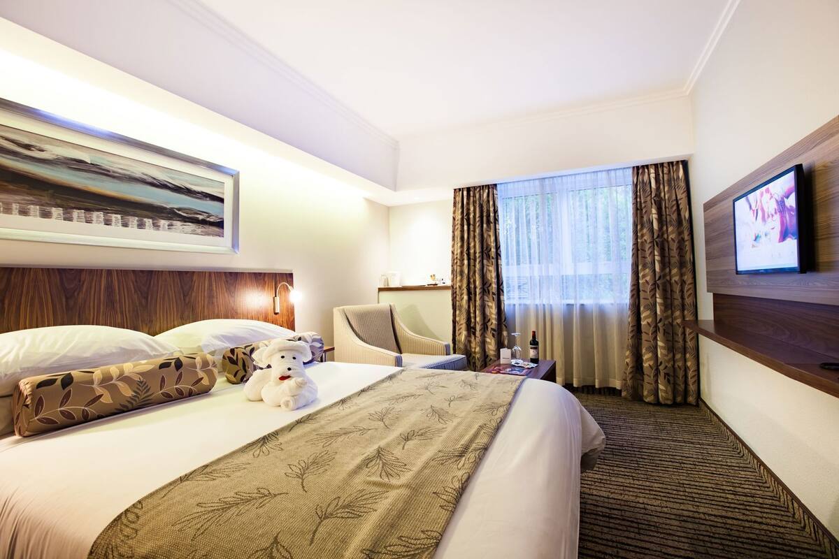 A hotel room with a bed, a chair, a TV, and a window with curtains.