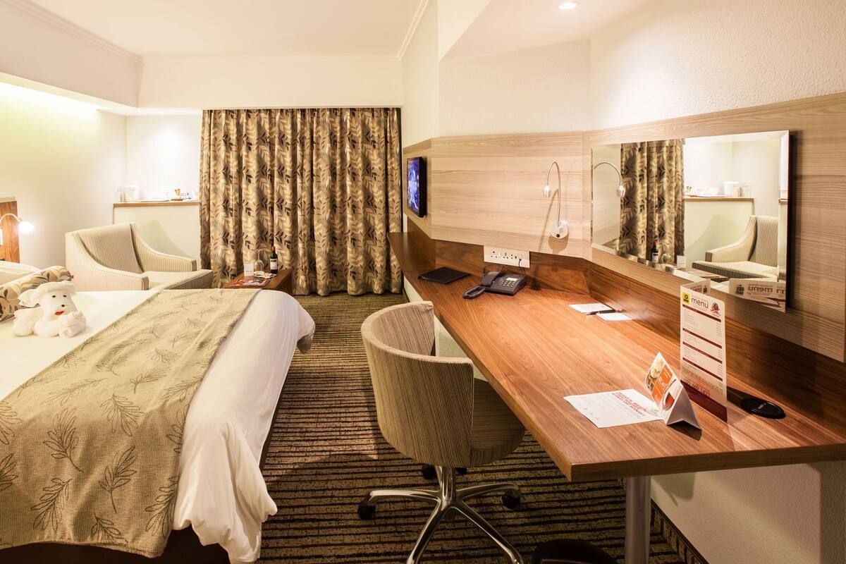 A hotel room with a bed, a desk, a chair, a telephone, a mirror, and a television.