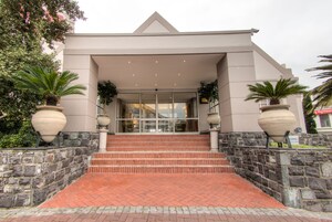 A building with a modern architectural style, featuring a set of stairs leading to a glass entrance, stone walls, and large planters with greenery.