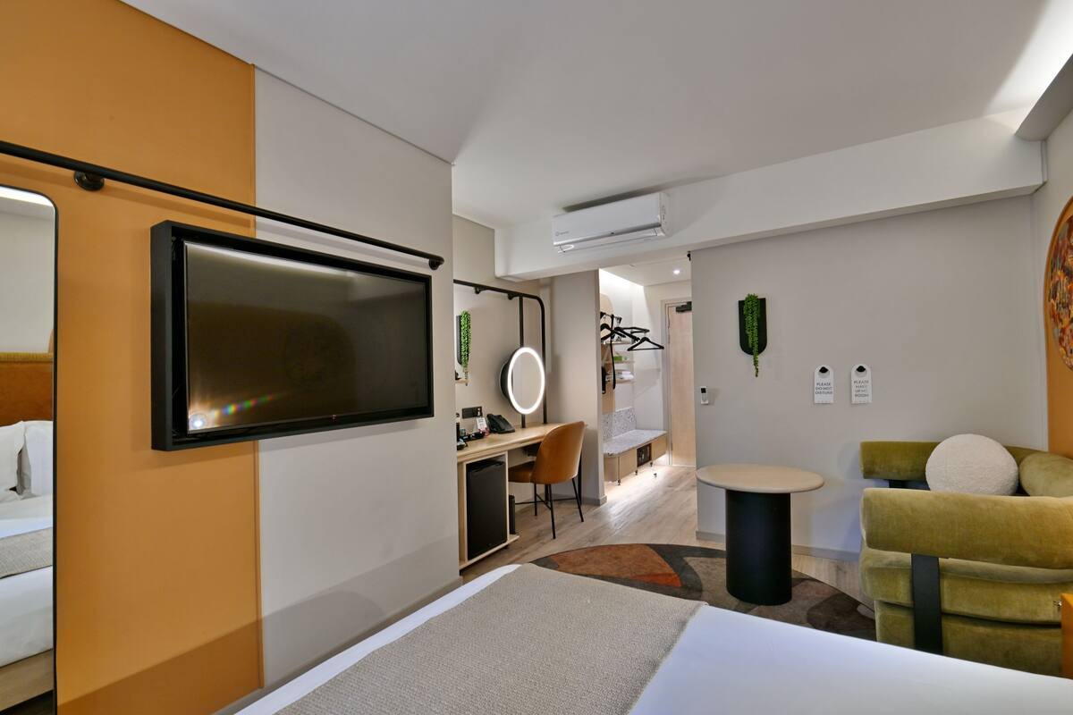 Ein Hotelzimmer mit einem Bett, einem Schreibtisch mit Computer, einem Sessel, einem Fernseher und einem kleinen Tisch.