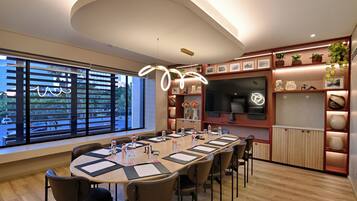A modern conference room with a long table, chairs, and a large window with blinds.