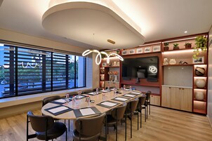 A modern conference room with a long table, chairs, and a large window with blinds.