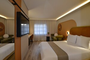 A hotel room with a large bed, a desk, a chair, and a television.