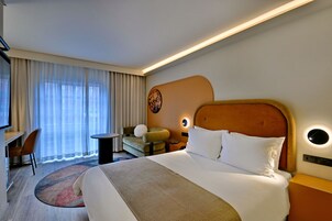 A hotel room with a large bed, a desk, a chair, a small table, and a sofa.