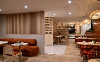 A modern restaurant interior with wooden paneling, round tables, and wicker pendant lighting.