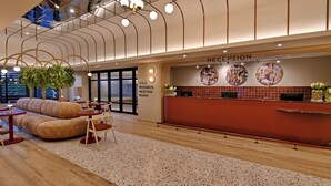 Un espace d’accueil moderne avec un comptoir rouge, un bureau d’accueil et un coin salon comprenant un canapé et des tables.