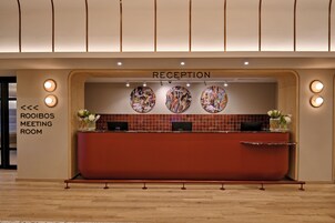 Un espace d’accueil doté d’un comptoir de réception en bois, de trois œuvres d’art murales de forme circulaire et d’un panneau indiquant la salle de réunion « Roibos ».