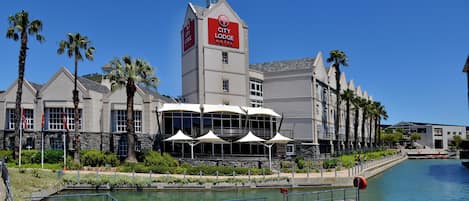 Un Hotel City Lodge con una torre destacada, un patio frente al agua y palmeras.
