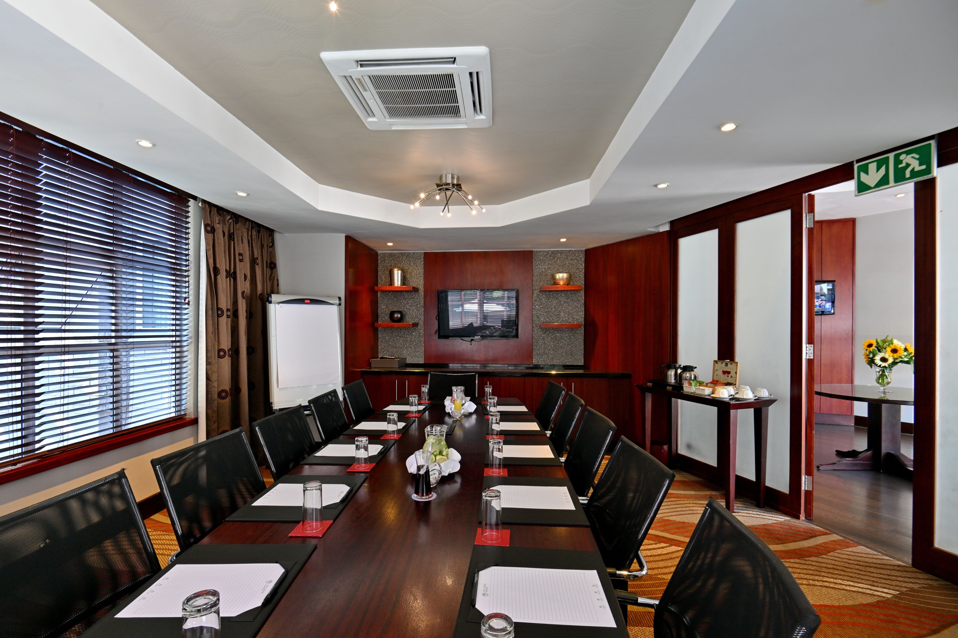 A conference room with a long table, chairs, a television, and a small table with a vase of flowers.